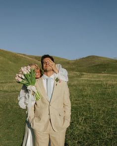 a man and woman standing in a field with flowers covering their eyes as they look at each other