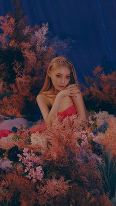 a woman in a red dress is surrounded by flowers and plants with her hands on her chest