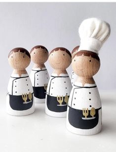 three wooden dolls are dressed in black and white outfits with a chef's hat on their head