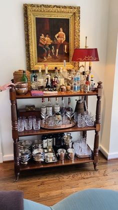 an old fashioned bar cart is full of liquor bottles and glassware in front of a painting on the wall