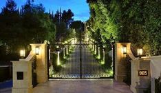 an entrance to a home with lights on the gate and trees in the back ground