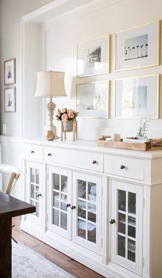 a dining room with white furniture and framed pictures on the wall above it's buffet table