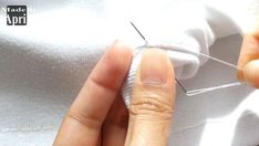 someone is sewing something on a white shirt with needles in their hands and the thread has been pulled through