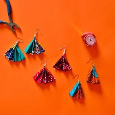 several different types of origami hanging from hooks on an orange surface with scissors and thread