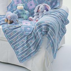 a crocheted blanket and two stuffed animals are on a white bed with a blue coverlet