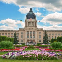 a large building with many flowers in the foreground and trees on the other side