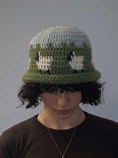 a person wearing a green and white crocheted hat with sheeps on it