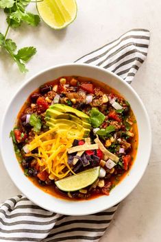 a white bowl filled with chili, cheese and avocado on top of a striped towel