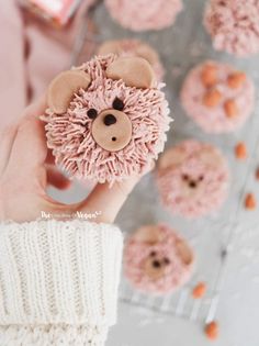 a person holding a teddy bear in front of some cupcakes on a rack