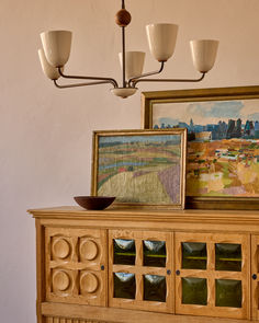 a painting hangs on the wall next to a wooden cabinet with glass doors and drawers