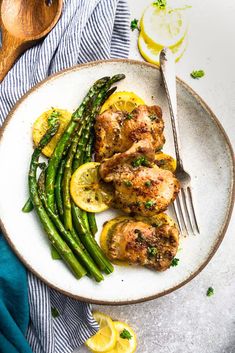 a plate with chicken, asparagus and lemons on it next to a fork