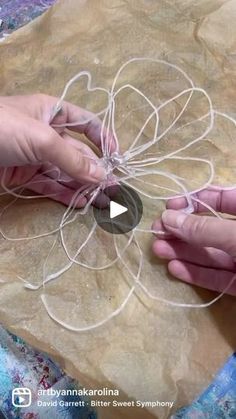 two hands are working on something with string and paper in the shape of a flower