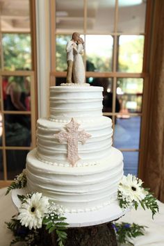 a wedding cake with two figurines on top and daisies around the edge