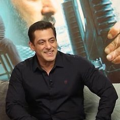 a man sitting on top of a couch in front of a movie poster and smiling