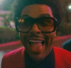 a man wearing glasses and a red jacket making a funny face with his tongue out