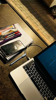 an open laptop computer sitting on top of a table next to a notebook and pencils