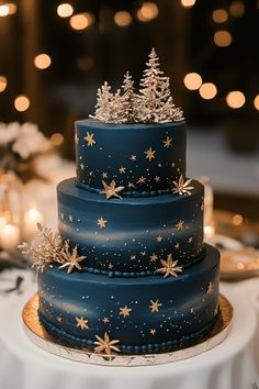 a three tiered blue cake with gold stars and trees on the top is sitting on a white tablecloth