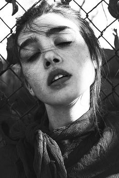 black and white photograph of a woman with her eyes closed behind a chain link fence