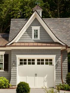 a gray house with two white garage doors on the front and one window in the back