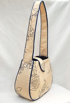 a handbag with flowers on it sitting on a white cloth covered surface, ready to be used as a purse or shoulder bag