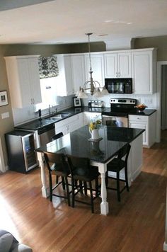 a kitchen with white cabinets, black counter tops and an island in front of the sink