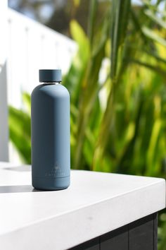 a blue water bottle sitting on top of a white table next to some green plants