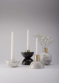 three white candles and two black vases with flowers in them on a grey background