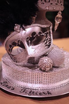 a silver masquerade on top of a cake with black feathers and beads around it