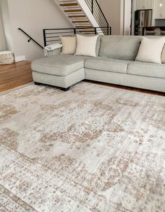 a living room with a large rug on the floor and stairs in the back ground