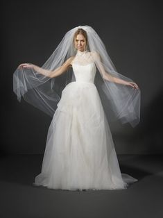 a woman in a white wedding dress with a veil over her head and hands behind her back