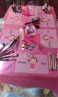 a pink table topped with lots of makeup and other items on top of the table