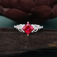 an engagement ring with a red stone surrounded by white cubicles on top of a piece of wood