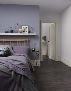 a bedroom with purple walls and wood flooring is pictured in this image, the bed has two pillows on it