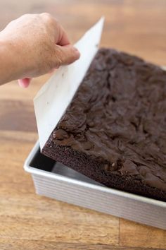 a person holding a piece of chocolate cake in front of a pan on a wooden table