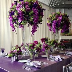 the table is set with purple and green flowers in vases on top of it