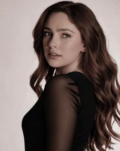 a woman with long brown hair wearing a black top and posing for a photo in front of a white background