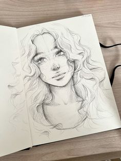 a drawing of a woman's face on top of a table next to an open book