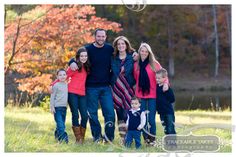 a family posing for a photo in front of some trees with fall foliage behind them