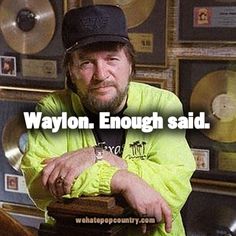 a man in a yellow jacket and black hat with his arms crossed, leaning on a record player