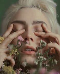 a woman with blonde hair holding her hands to her face while surrounded by wildflowers