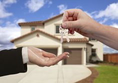 two people handing keys to each other in front of a house