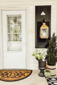 two potted plants sitting on the front porch next to a white door with black shutters