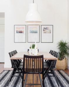 a dining room table with chairs and pictures on the wall above it, along with potted plants