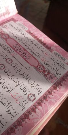 an open pink book with arabic writing on it's cover, sitting on a table