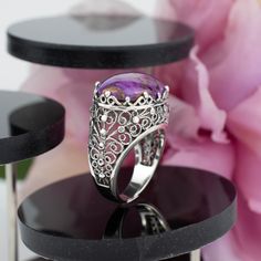 "Indulge in the allure of our Handcrafted Sterling Silver Dome Cocktail Ring, a masterpiece of filigree artistry. Meticulously handcrafted from 925 sterling silver, this statement ring features a captivating 13x18 mm cabochon or faceted oval cut gemstone, available in the natural, soothing Rhodonite, the vibrant Purple Mohave Turquoise, or the regal Amethyst. The ring face length is 0.80 inches and the width is 0.60 inches  Each gemstone holds its unique charm: Rhodonite, a symbol of compassion and love; Purple Mohave Turquoise, a beacon of creativity and protection; and Amethyst, a stone of clarity and spirituality. Our commitment to impeccable craftsmanship extends to fit, with 16 different sizes ranging from a dainty size 5 to a luxurious 12.5, including half sizes. Searching for the pe Silver Turquoise Ring With Accent Stones, Fine Jewelry Silver Turquoise Ring With Accent Stones, Fine Jewelry Turquoise Ring With Accent Stones In Silver, Elegant Amethyst Cabochon Ring, Fine Jewelry Purple Cabochon, Spiritual Opal Ring Gift, Oval Amethyst Jewelry Collectible, Fine Jewelry Amethyst Cabochon, Elegant Turquoise Gemstone Ring For Formal Occasions