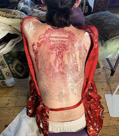 the back of a woman's body is covered in tattoos and red cloths