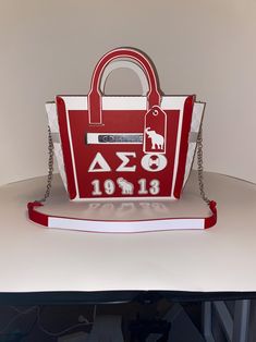 a red and white handbag sitting on top of a table next to a book