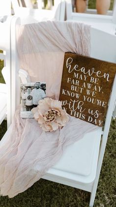 a wooden sign sitting on top of a white chair next to a pink blanket and flower