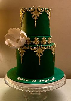 a three tiered green cake with gold decorations and a white flower on the top