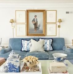 a living room with blue couches and pictures on the wall above them in gold frames